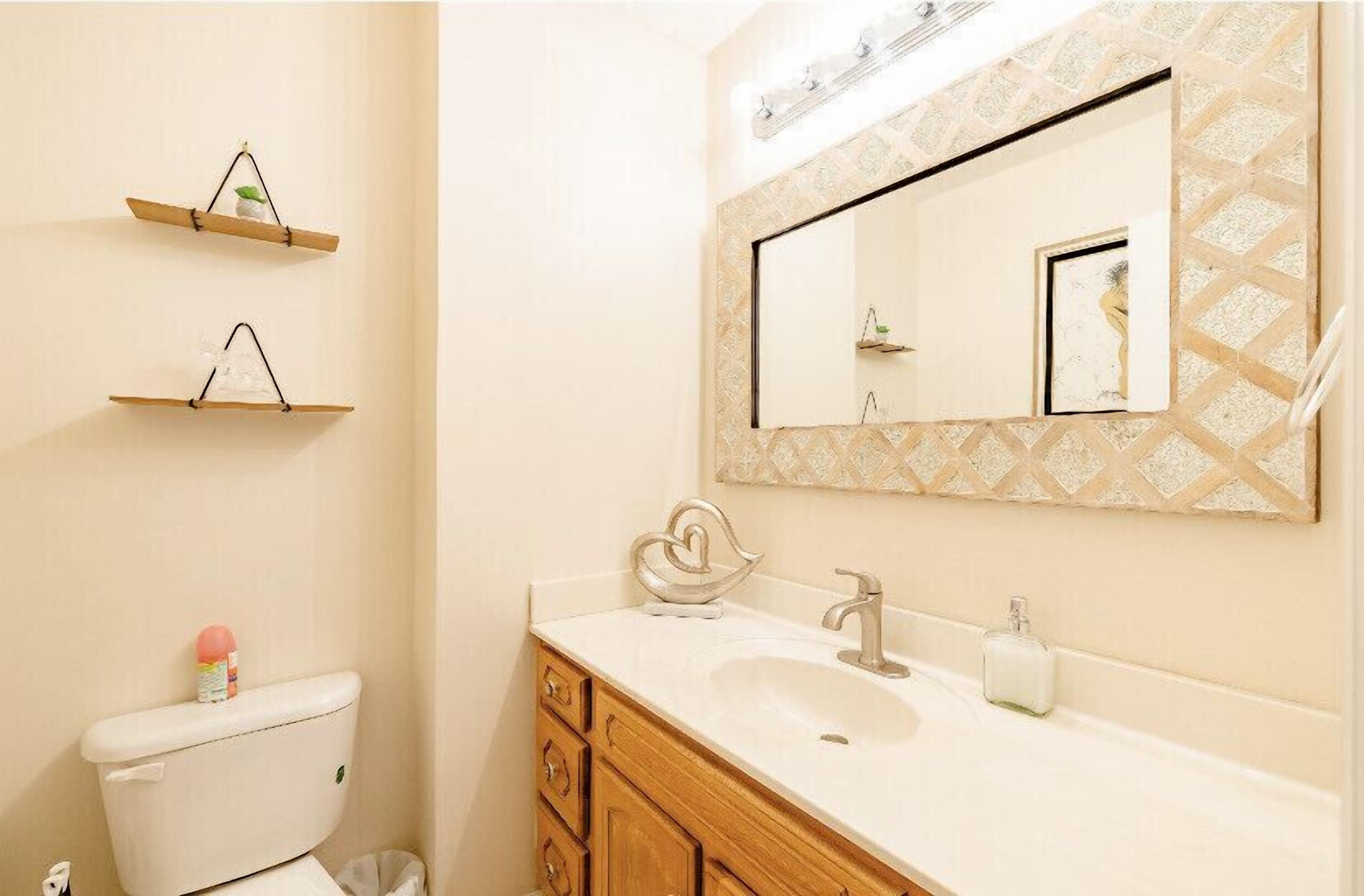 A bathroom with a toilet, a sink, wooden cabinets, and two shelves with decorative items.