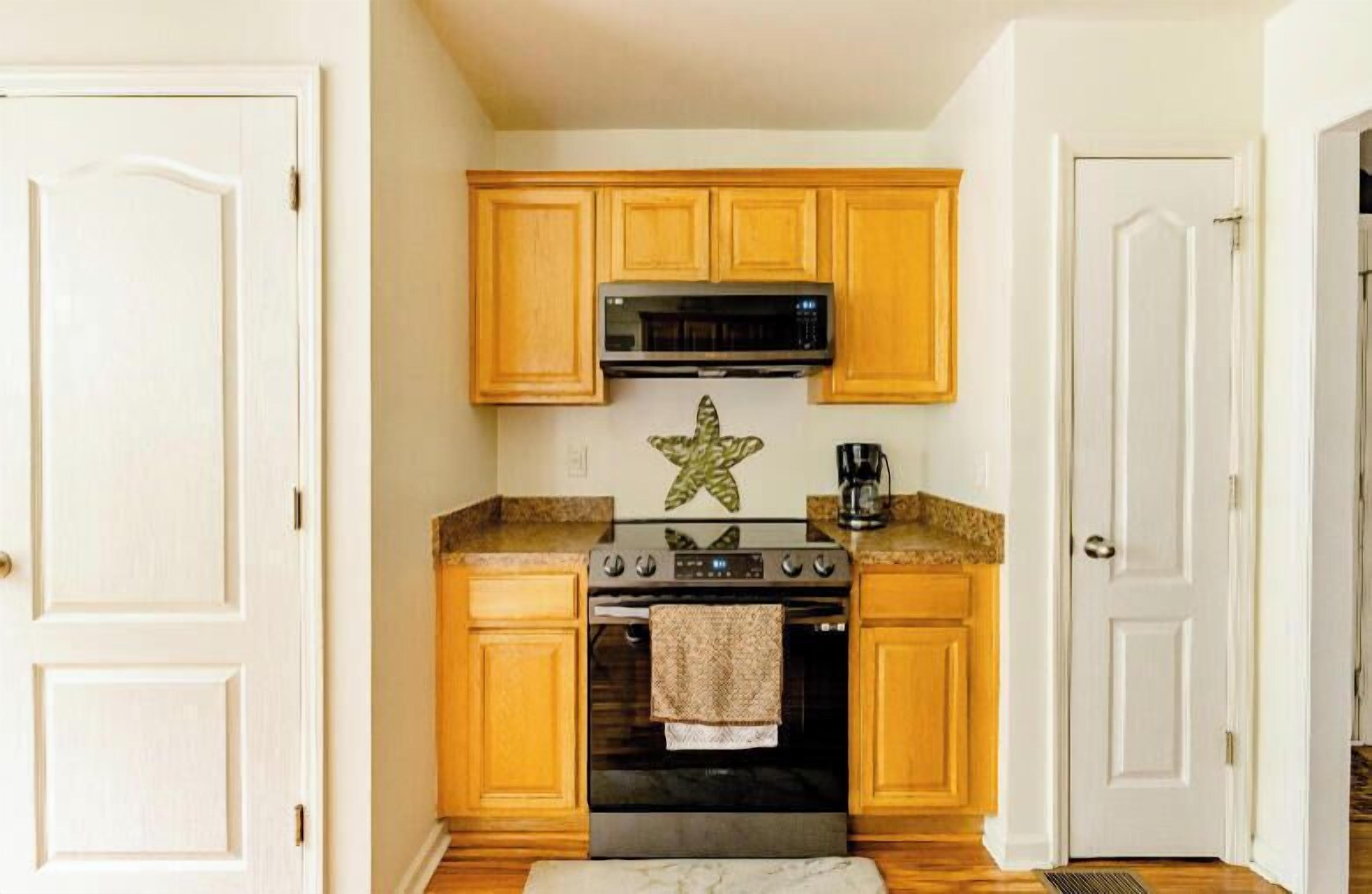 Una cocina compacta con armarios de madera, un microondas, una estufa y una cafetera.