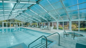 Area piscina coperta con tettoia in vetro, poltrone relax e una piccola vasca idromassaggio.