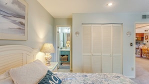 Una camera da letto con un letto, un comodino, una lampada, un armadio e un bagno visibile attraverso una porta aperta.