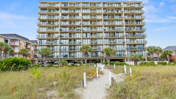 A multi-story hotel with balconies, a sandy path leading to the entrance, and palm trees. - Spacious family-friendly oceanfront condos w/easy beach access in North Myrtle Beach (North Myrtle Beach)