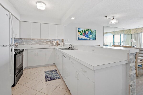 A modern kitchen with white cabinetry, a large island, and a painting above the sink.