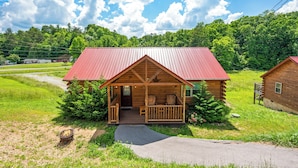Une cabane en bois avec un toit rouge, une véranda et un foyer extérieur à l’avant.