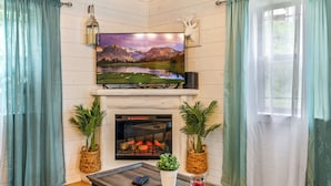 Un salon chaleureux avec une cheminée, un téléviseur fixé au mur et deux plantes en pot.