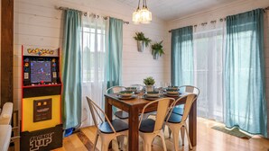 Un espace repas comprenant une borne d’arcade Pac-Man, une table en bois et des chaises.