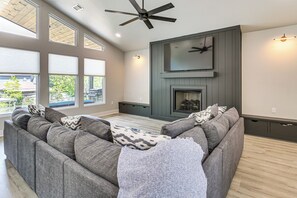 A modern living room with a sectional sofa, a fireplace, and a ceiling fan. - Lakefront Hot Springs Home w/ Private Dock (Hot Springs)