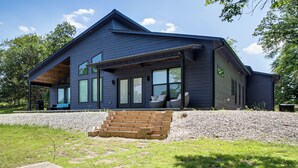 A modern two-story house with a covered porch, large windows, and a brick staircase leading to the entrance. - Lakefront Hot Springs Home w/ Private Dock (Hot Springs)