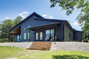 Une maison moderne à deux étages, dotée d’un porche abrité, de grandes fenêtres et d’un escalier en briques menant à l’entrée.