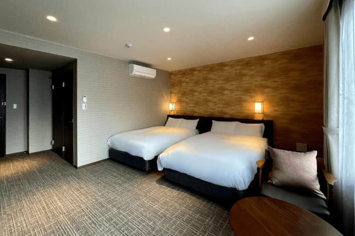 A hotel room with two beds, a wooden headboard, a small table, and a wall-mounted air conditioner.