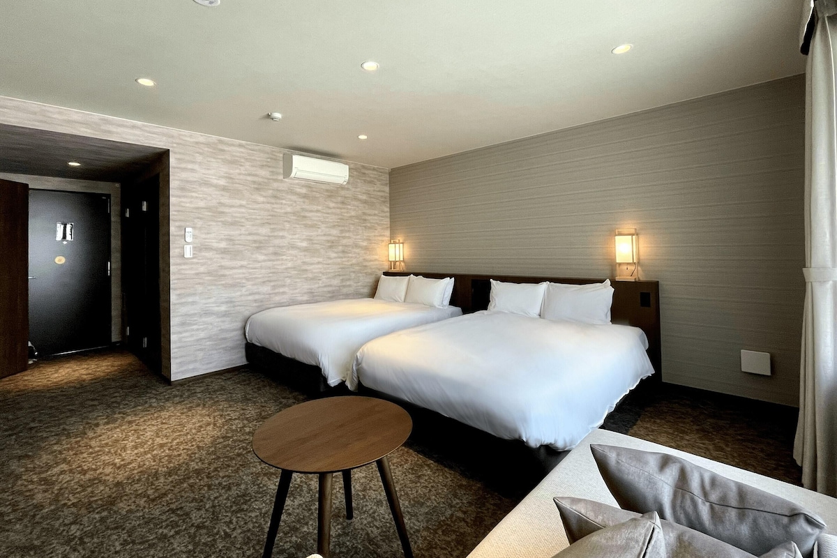 Una habitación de hotel con dos camas, una mesita redonda pequeña y un sofá.