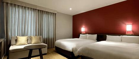 Ein Hotelzimmer mit zwei Betten, einer Schlafcouch, einem kleinen Tisch und einer roten Akzentwand.