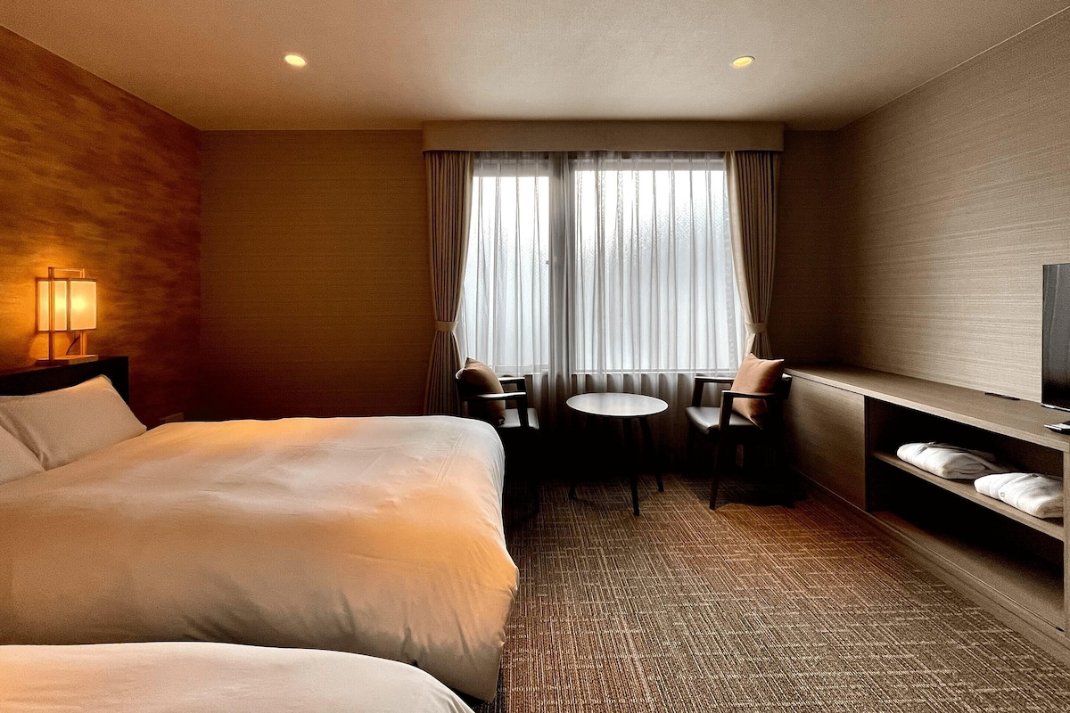 Habitación de hotel con una cama grande, un escritorio con silla, un televisor y una ventana con cortinas.