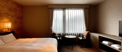 A hotel room with a large bed, a desk with a chair, a television, and a window with curtains.