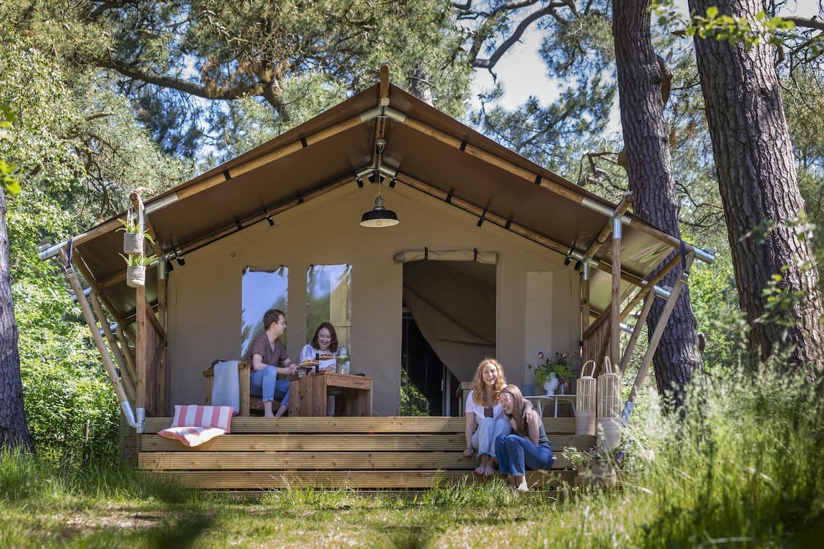 Une cabane en bois dotée d’un porche couvert, d’un banc et d’une table agrémentée d’un coussin à rayures rouges et blanches.