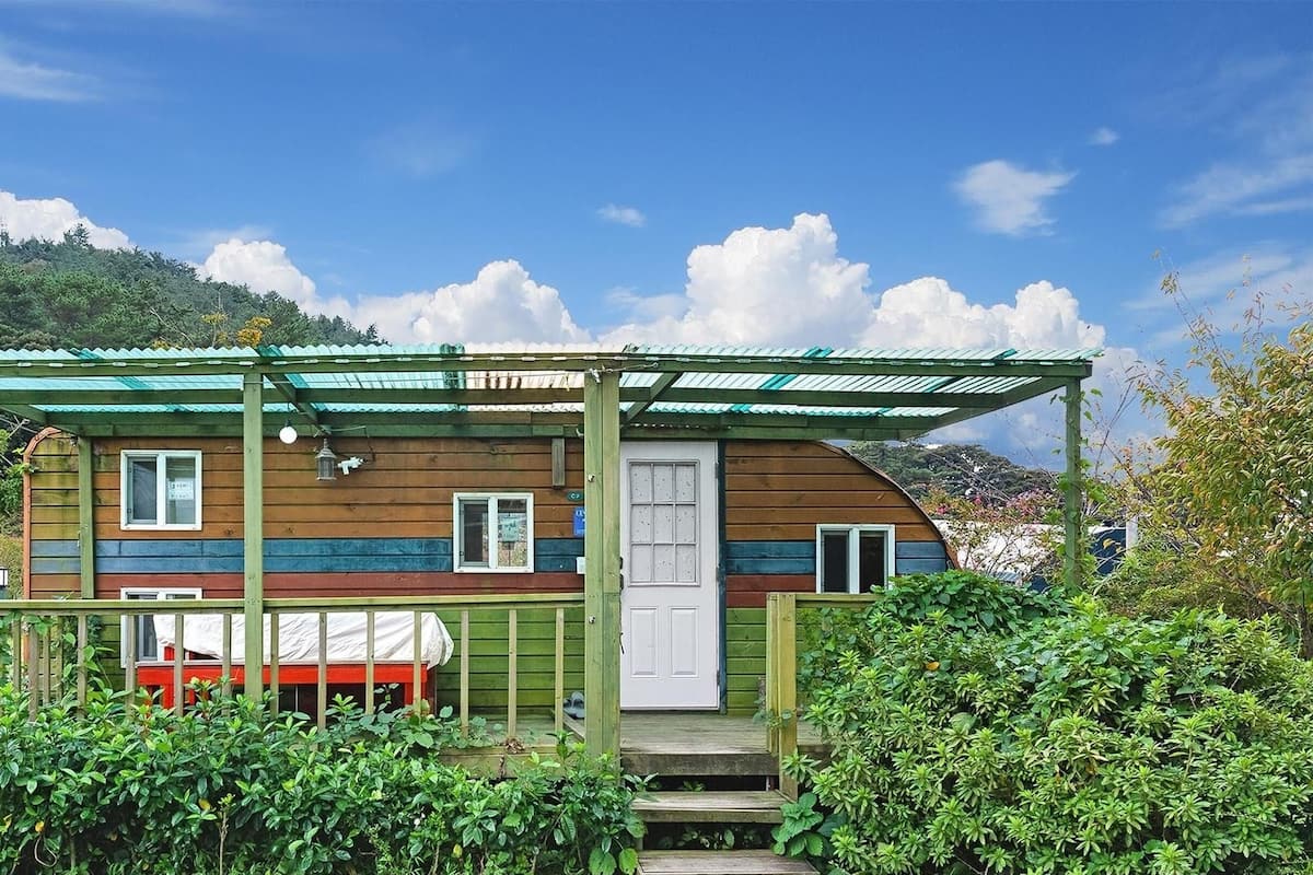Une cabane en bois avec un toit vert et une véranda couverte, entourée d’une végétation luxuriante.