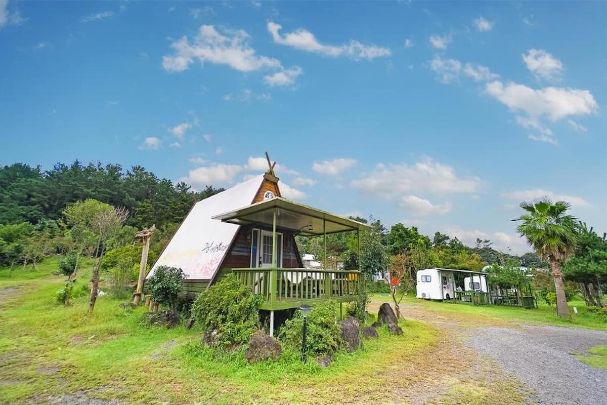 Une maison unique, dotée d’un toit en pente et d’une terrasse en bois, entourée d’une végétation luxuriante et sous un ciel dégagé.