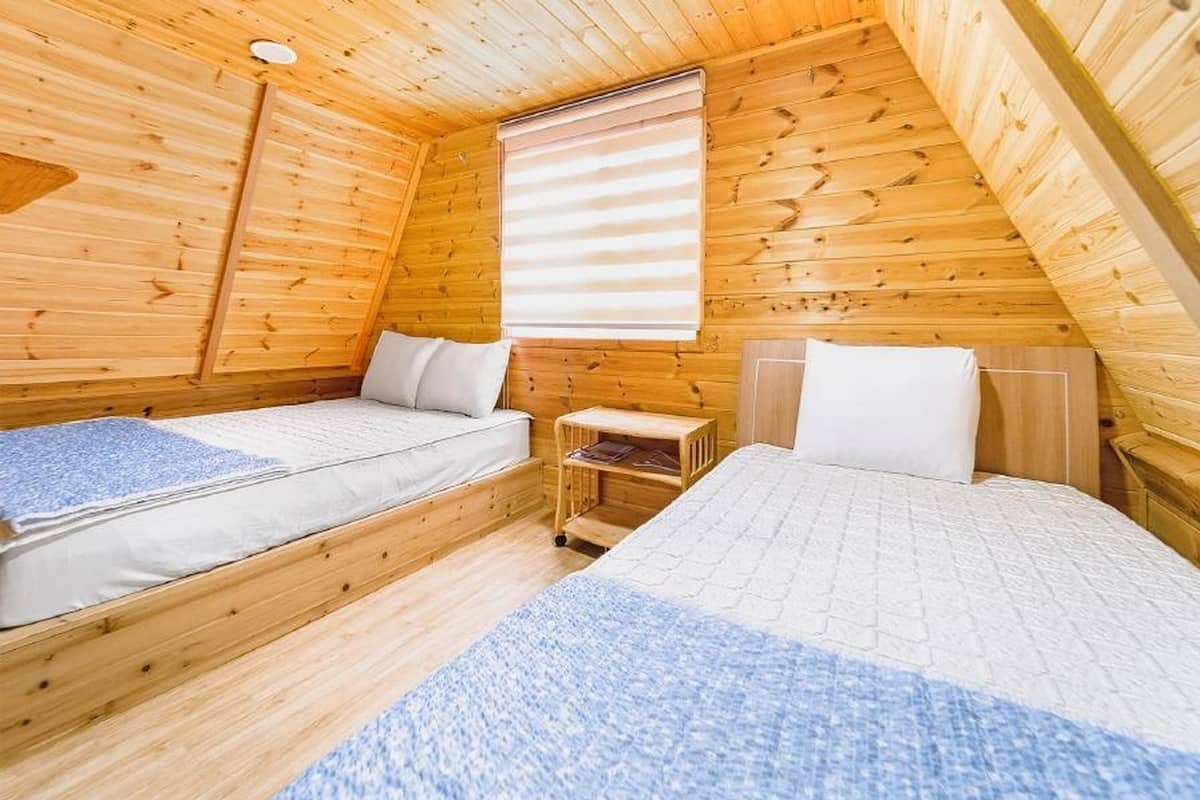 Une petite pièce chaleureuse aux murs en bois et au plafond en pente. On y trouve deux lits avec du linge de lit blanc, et une petite table de chevet en bois placée entre les deux.