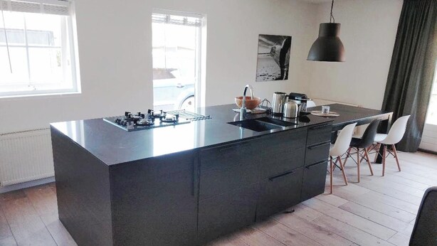 Une cuisine moderne dotée d’un grand îlot central, d’un évier intégré et d’un coin repas avec des chaises blanches.