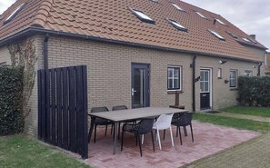 Une maison à deux étages, avec un toit en tuiles, une façade en briques et un patio aménagé avec une table et des chaises.