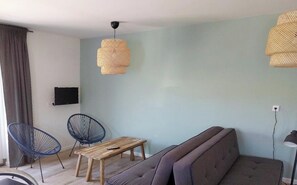 Un salon moderne avec un canapé, deux fauteuils bleus, une table en bois et deux suspensions en fibres tressées.