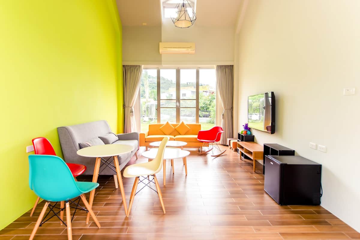 Una sala de estar luminosa con un sofá, sillas, una mesita, un televisor y un refrigerador.