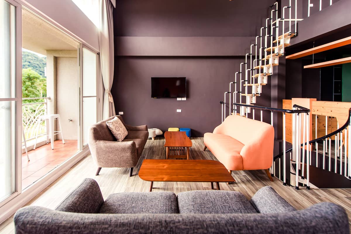 Una sala moderna con un sofá, un sillón y una mesa de centro. Se observa una escalera con barandilla a la derecha.