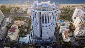 A high-rise hotel with a curved facade, located near a beach with palm trees and a clear view of the ocean. - Panorama Luxstay Nha Trang (Nha Trang)