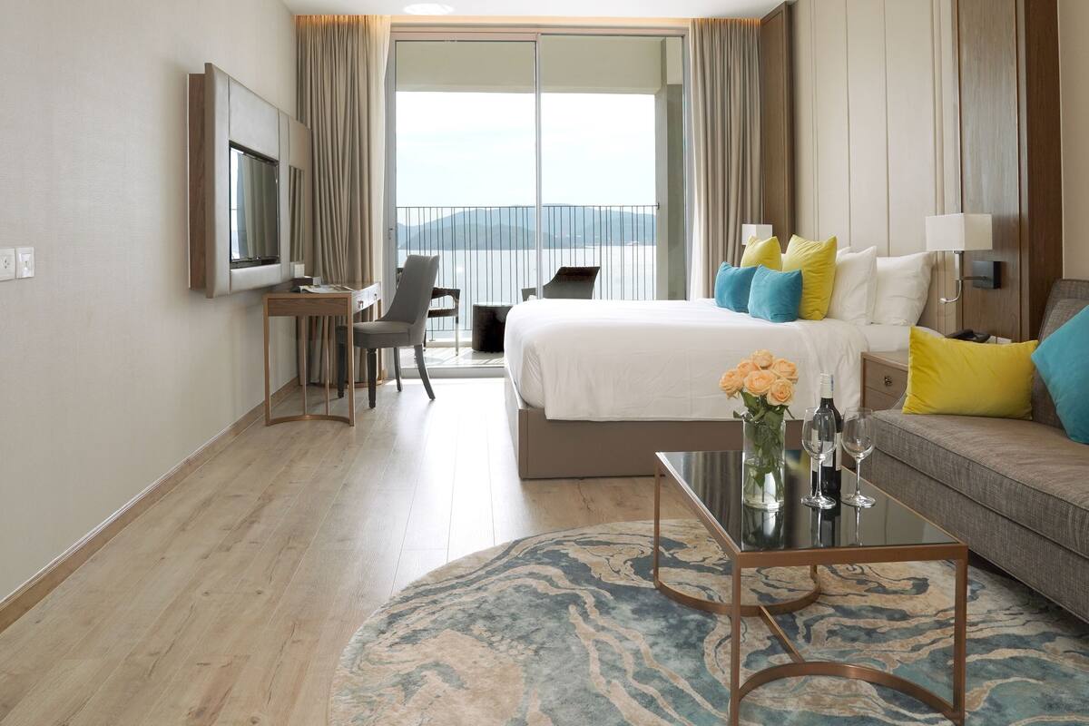 Une chambre d’hôtel avec un lit, un canapé, une télévision, un bureau et un balcon offrant une vue.