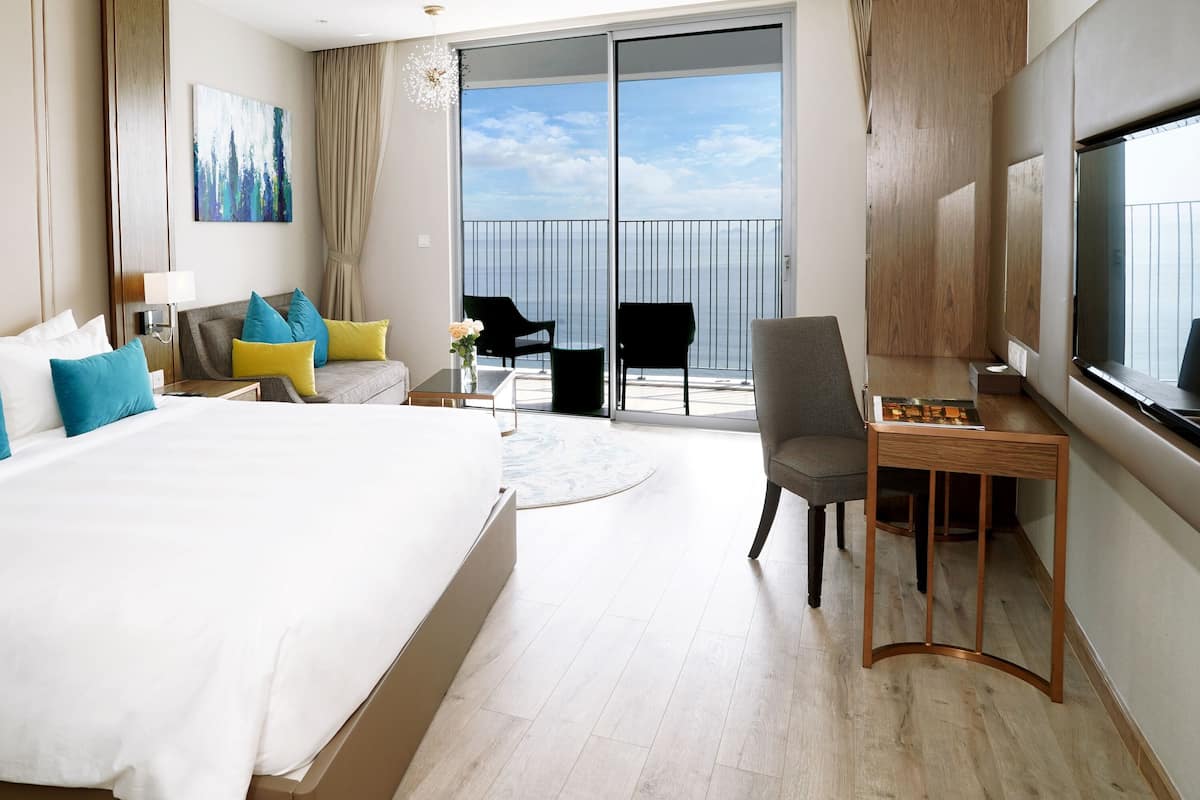 Une chambre d’hôtel avec un grand lit, un bureau, une chaise, une télévision et un balcon avec vue.