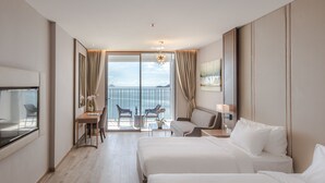 A hotel room with two beds, a desk with chairs, a TV, and a balcony with a view of the sea. - Panorama Luxstay Nha Trang (Nha Trang)