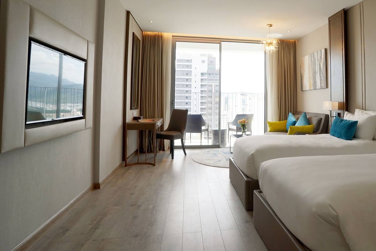 Une chambre d’hôtel avec deux lits, un bureau, une chaise et une vue sur la ville.