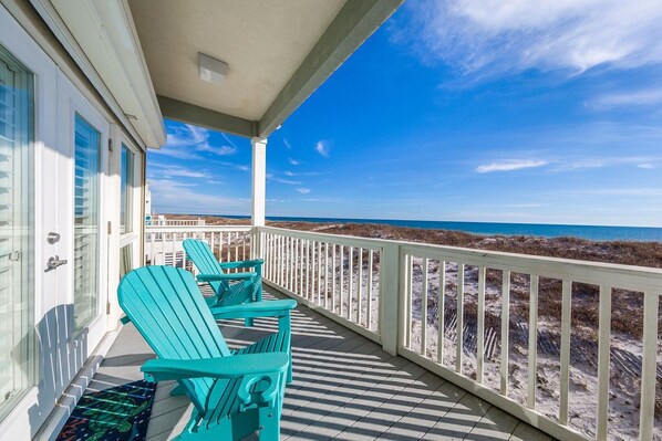 A balcony with turquoise Adirondack chairs, a white railing, and a view of the beach and ocean. - Del Sol Beach House | Rare Dog Friendly Beachfront Home | My Beach Getaways (Gulf Shores)