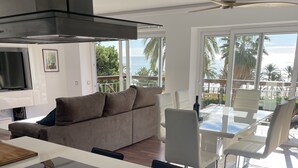 Et moderne køkken med indbygget ovn, et spiseområde med et glasbord, og en balkon med udsigt til palmer.
