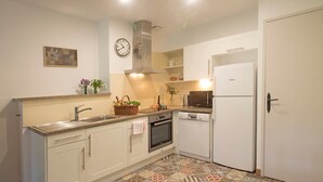 A kitchen with white cabinets, a stainless steel range hood, a Bosch refrigerator, and a patterned tile floor. - Maison des Cyprès (N°3) (Marcorignan)