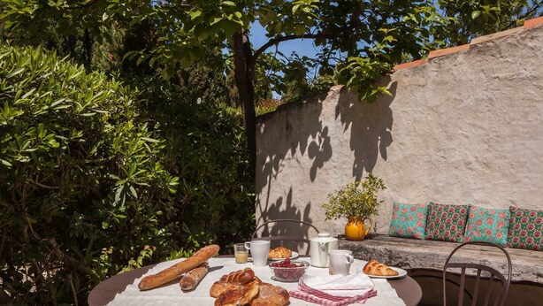 Un espacio al aire libre con zona de comedor y una mesa preparada para el desayuno, incluyendo pan, bollería y una cafetera.
