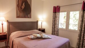 Una cama bien hecha con almohadas estampadas, un cabecero, lámparas de noche y un cuadro en la pared.