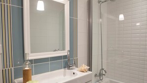Un baño con un lavamanos blanco, una mampara de ducha de vidrio y un espejo sobre el lavamanos.