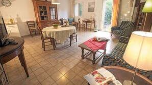 Una sala de estar con comedor, un sofá, una mesa con mantel rojo y una lámpara.
