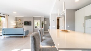 A modern kitchen with a long countertop, a blue sofa, and a dining area. - Apartamentos Ponent MHM (Cala Ratjada)