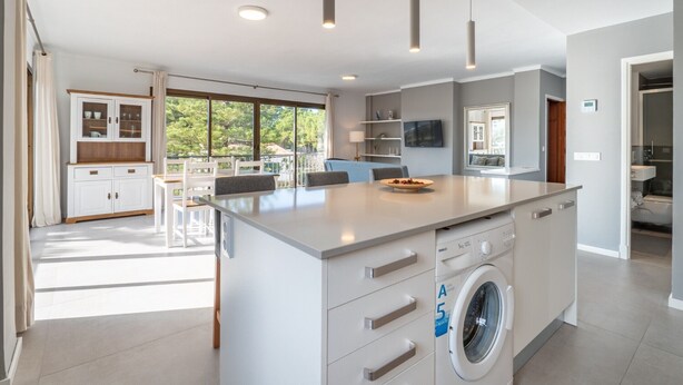 A modern kitchen with a central island, built-in appliances, and a dining area with a view. - Apartamentos Ponent MHM (Cala Ratjada)