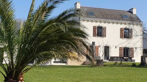 Una casa de dos pisos con fachada de piedra, contraventanas de madera y un césped cuidado.