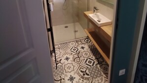 Un baño moderno con cabina de ducha de vidrio, tocador de madera y baldosas de suelo con diseño.