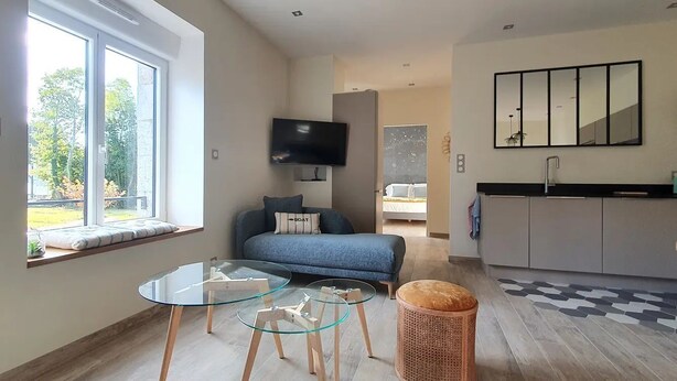 Un espacio habitable moderno y funcional con mesa de vidrio, sofá, televisor y área de cocina.