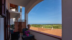 A balcony with wicker furniture, a potted plant, and a view of a tiled roof and greenery.