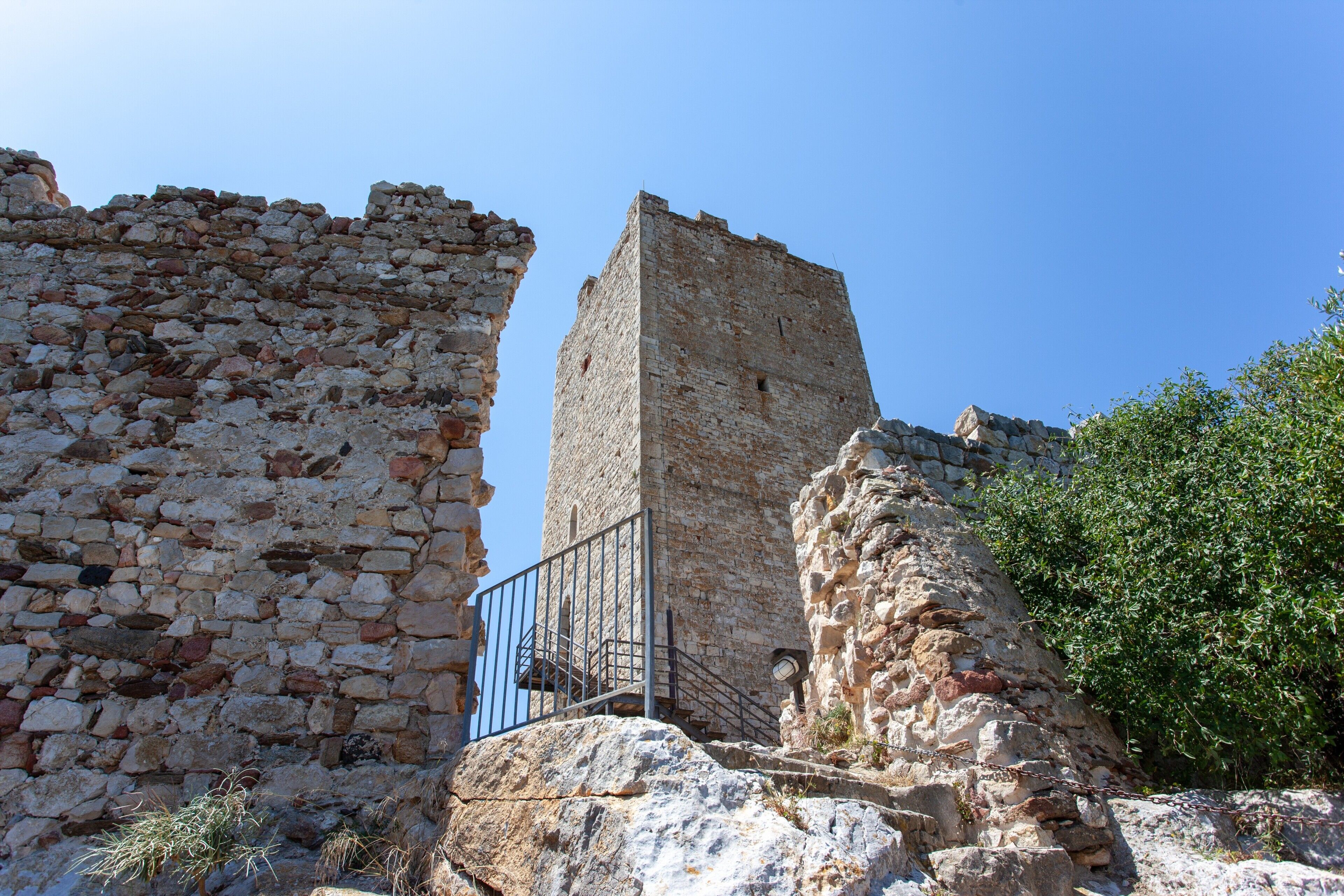 An ancient stone structure with a tall tower and a staircase leading to a balcony.
