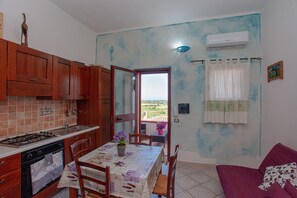 Une cuisine avec des meubles en bois, une table à manger avec des chaises, un canapé violet et une vue à travers une porte vitrée.
