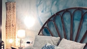 A bed with patterned pillows, a headboard, a nightstand with a lamp, and a textured wall.