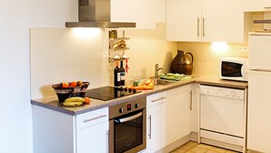 A modern kitchen with white cabinets, a stainless steel range hood, a microwave, an oven, and a sink.