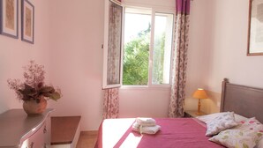 A bedroom with a bed, a nightstand, a lamp, a dresser, and a window with curtains.