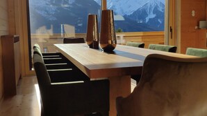 Un comedor con una mesa y sillas, ventanas amplias con vista a la montaña y vigas de madera en el techo.